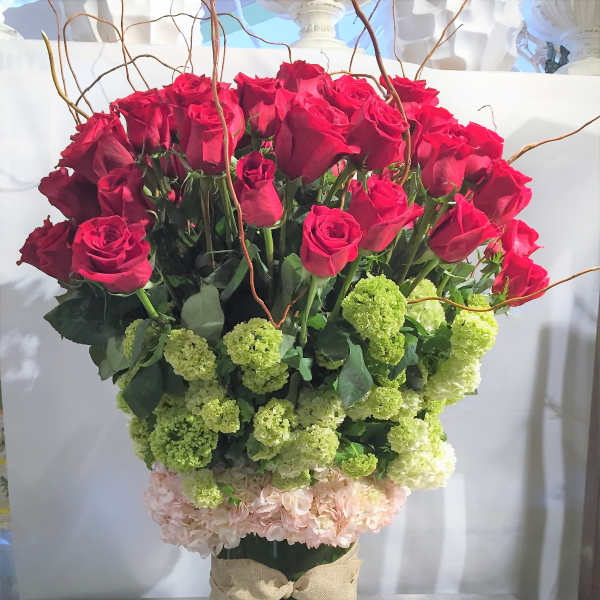 Tall arrangement of red roses and green hydrangeas in a glass vase