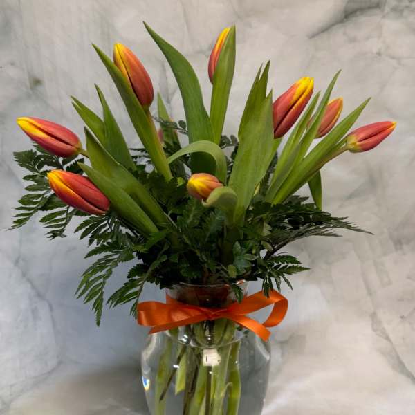 Orange and yellow tulips arranged in a clear glass vase with a ribbon.