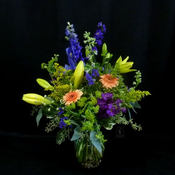 Mixed bouquet of lilies, gerbera daisies, and purple flowers in a glass vase