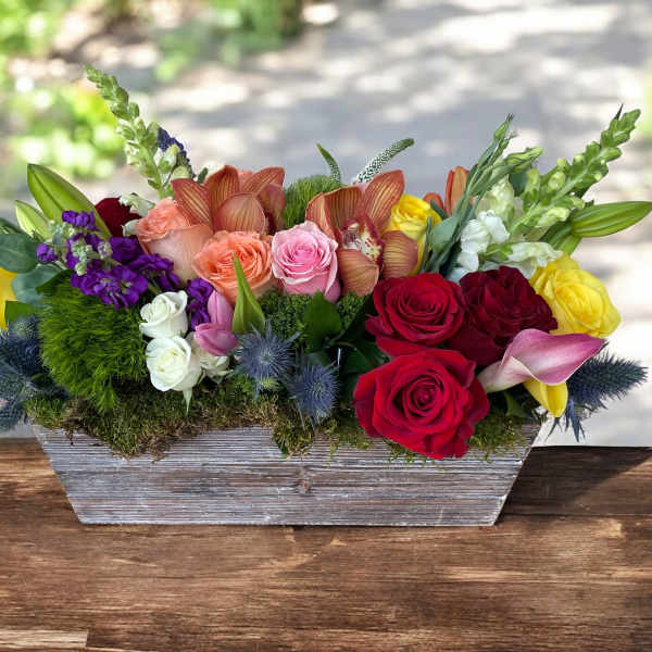 Mixed bouquet of roses, orchids, lilies, and snapdragons in a wooden planter
