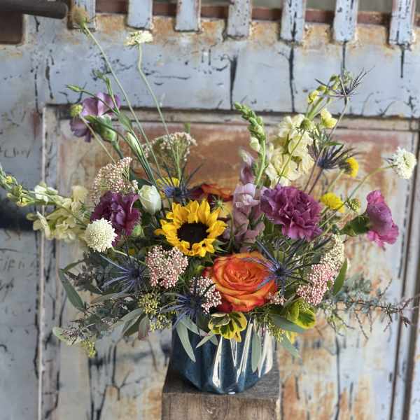 Mixed bouquet with a sunflower, orange rose, and purple blooms in a vase