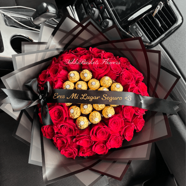 Round bouquet of red roses with gold-wrapped chocolates and black ribboned wrapping on a car seat.