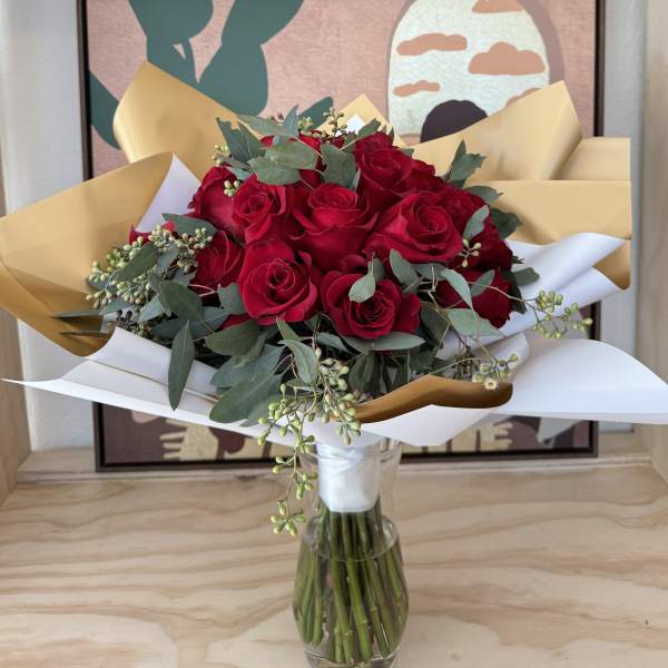 Bouquet of red roses in a clear glass vase with white and gold wrap