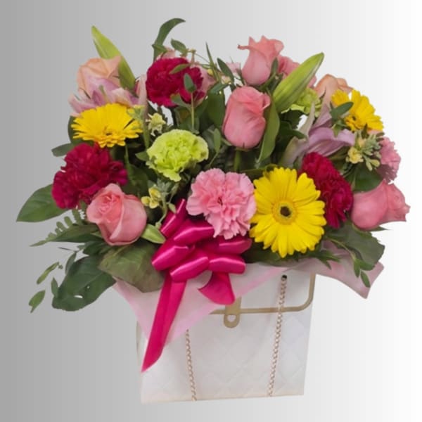 Mixed bouquet of pink roses, yellow daisies, and carnations in a gift bag