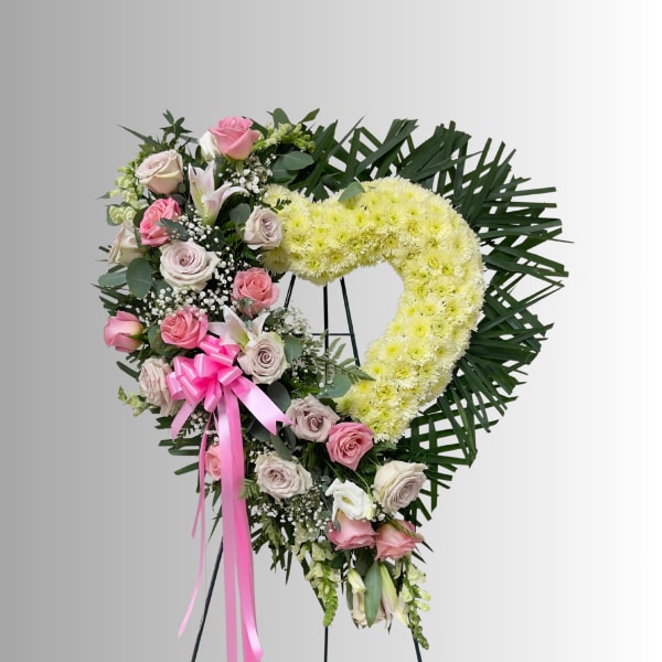 Heart-shaped floral wreath with pink roses and pale yellow flowers on a stand