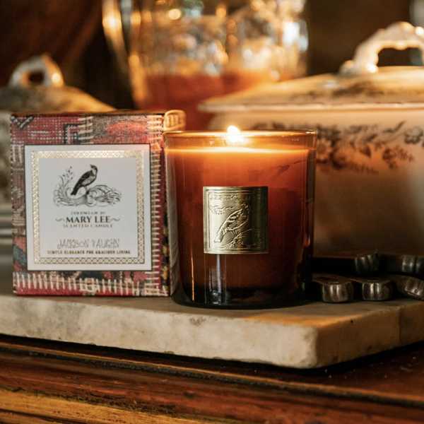 Lit amber candle in a glass jar beside a decorative candle box