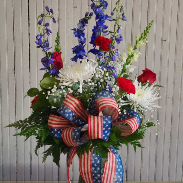 Tall red, white, and blue floral arrangement in a glass vase with patriotic ribbon