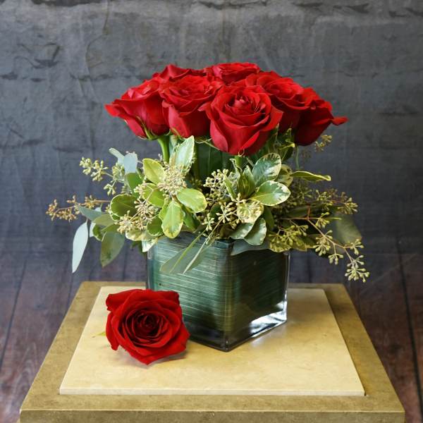 Red roses arranged in a square glass vase with greenery
