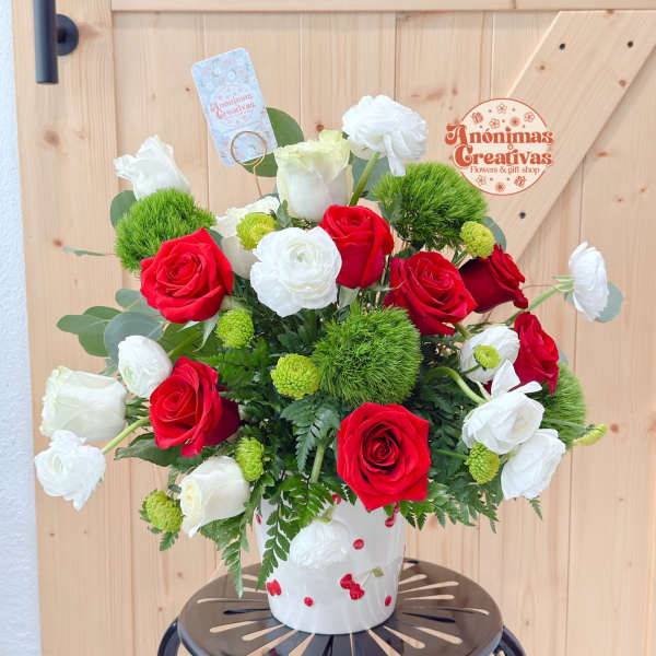 Red and white roses arranged in a white vase with green accents