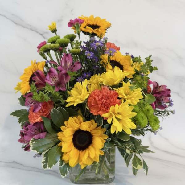 Bright mixed bouquet with sunflowers, daisies, and alstroemeria in a glass vase