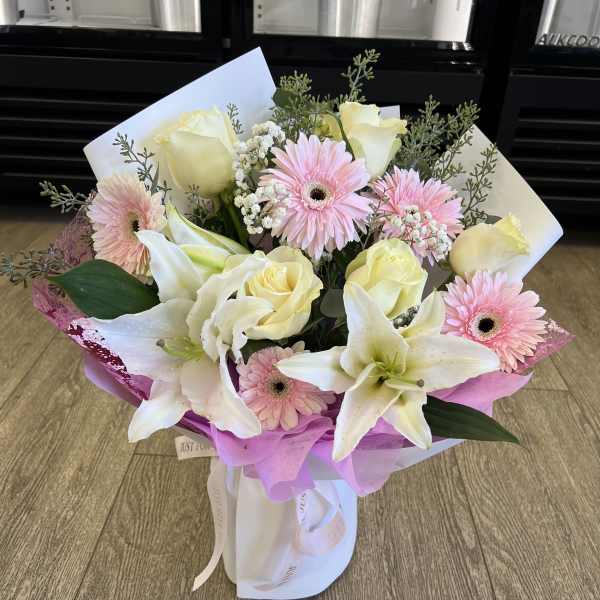 Bouquet of pale yellow roses, pink gerbera daisies, and white lilies wrapped in pink paper