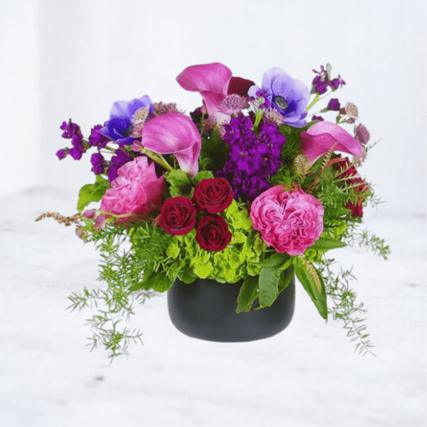 Mixed bouquet with pink calla lilies, roses, and purple flowers in a black vase