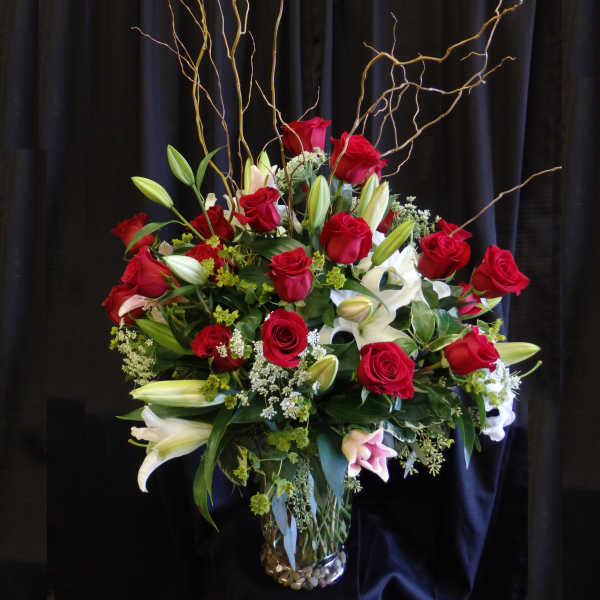 Red roses and white lilies in a glass vase with curly branches