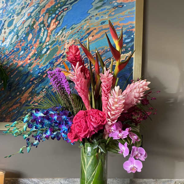 Tropical bouquet in a tall glass vase with pink orchids and bright mixed blooms