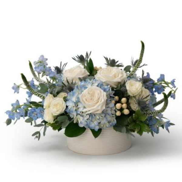 Low arrangement of white roses and blue hydrangeas in a round white ceramic vase
