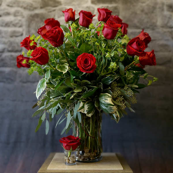 Red roses arranged in a clear glass vase with greenery