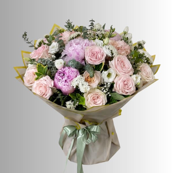 Bouquet of pale pink roses and peonies wrapped in beige paper with a ribbon