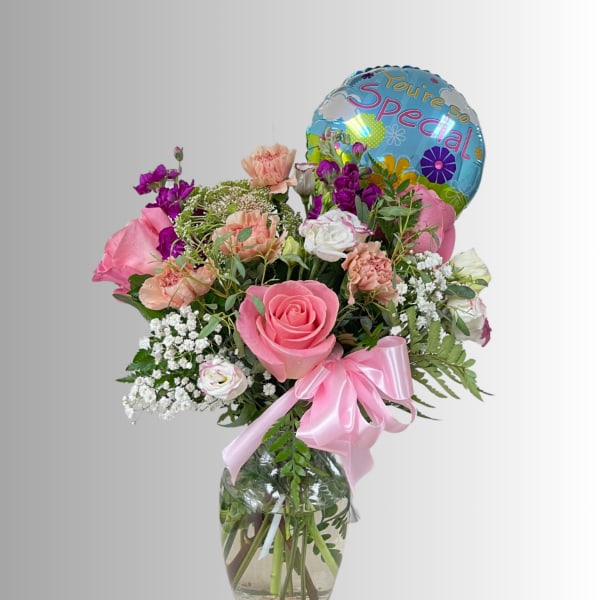 Pink and peach flower bouquet in a glass vase with a blue balloon