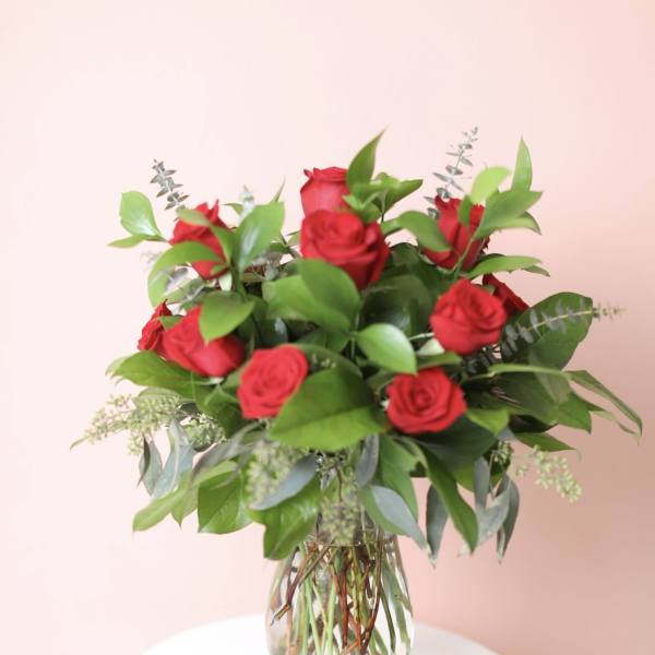 Red roses arranged in a clear glass vase with greenery