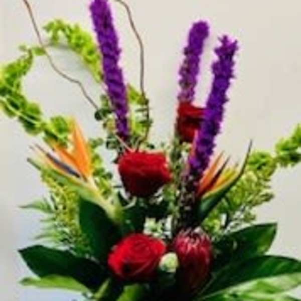 Tropical flower arrangement with red roses and purple spikes in a glass vase