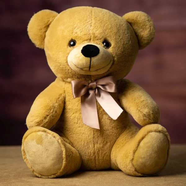 Golden brown teddy bear with a satin bow sitting on a matching fabric surface