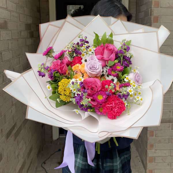 Large bouquet of pink, purple, and yellow flowers wrapped in white paper