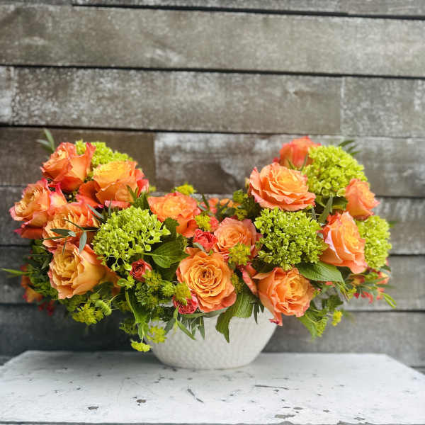 Orange roses and green hydrangeas in a white bowl vase