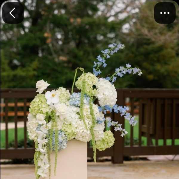 Wedding floral arrangement with white, pale green, and light blue flowers on a pedestal