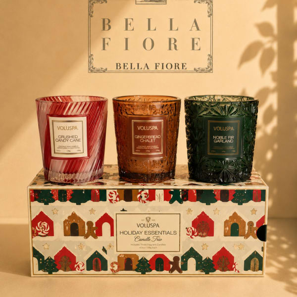 Three scented candles in decorative glass holders on a holiday gift box