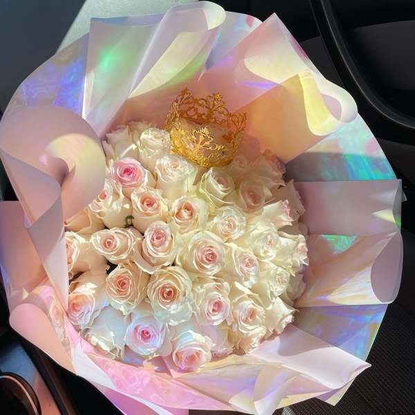 Bouquet of pale pink and white roses wrapped in iridescent paper with a gold crown
