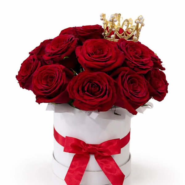 Red roses in a white hat box with a red ribbon and small crown topper