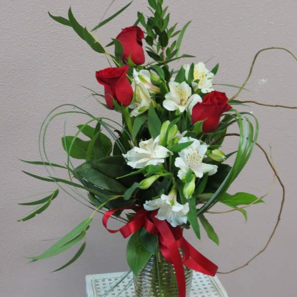 Red roses and white alstroemeria in a glass vase with a red ribbon