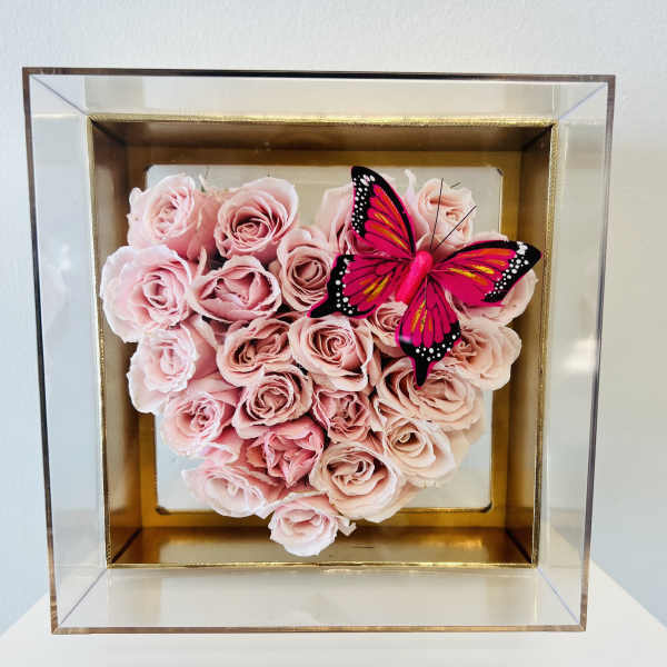 Pink roses arranged in a square shadow box with a butterfly accent