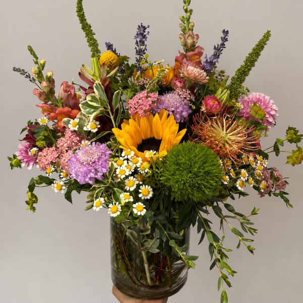 Mixed bouquet with a sunflower, daisies, and pink blooms in a glass vase
