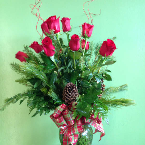 Red roses arranged in a glass vase with pinecones and plaid ribbon