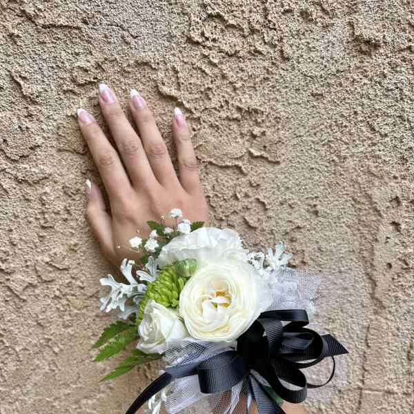 White floral wrist corsage with black ribbon on a hand