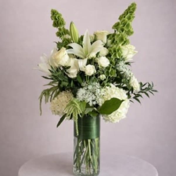White lilies and hydrangeas in a tall glass vase with green accents