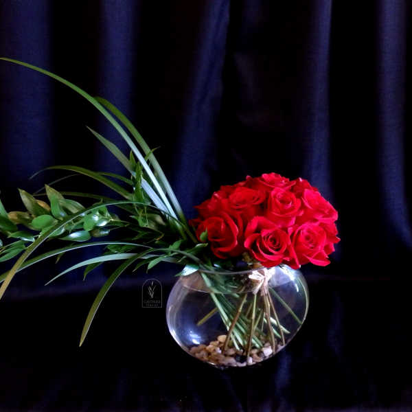 Red roses arranged in a round glass vase with long green leaves