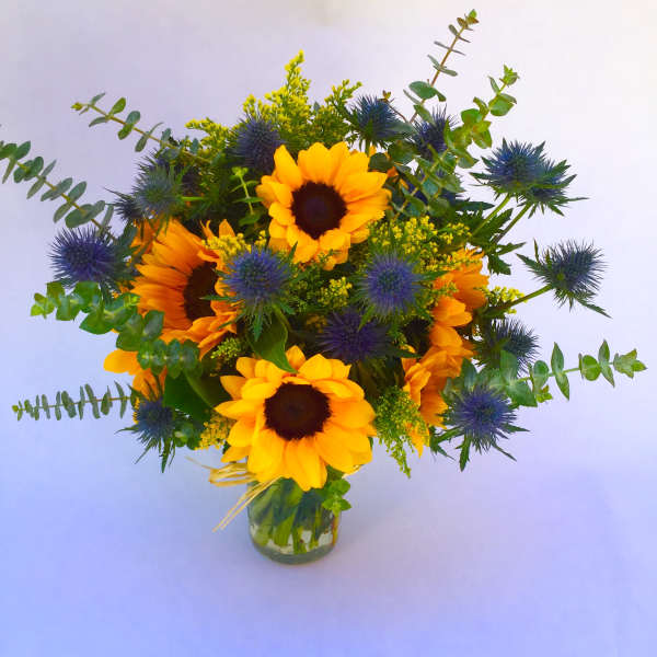 Sunflowers and blue thistle in a clear glass vase