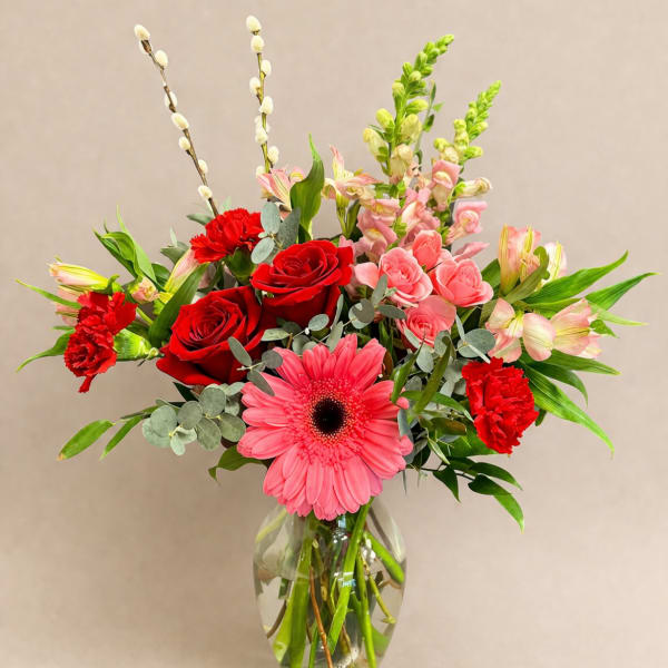 Mixed bouquet with red roses, pink gerberas, and carnations in a glass vase