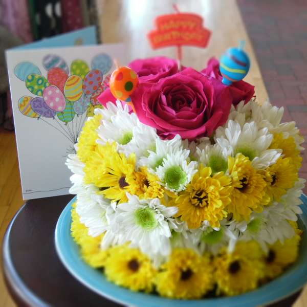 Pink roses and yellow-white daisies in a blue bowl with balloon picks