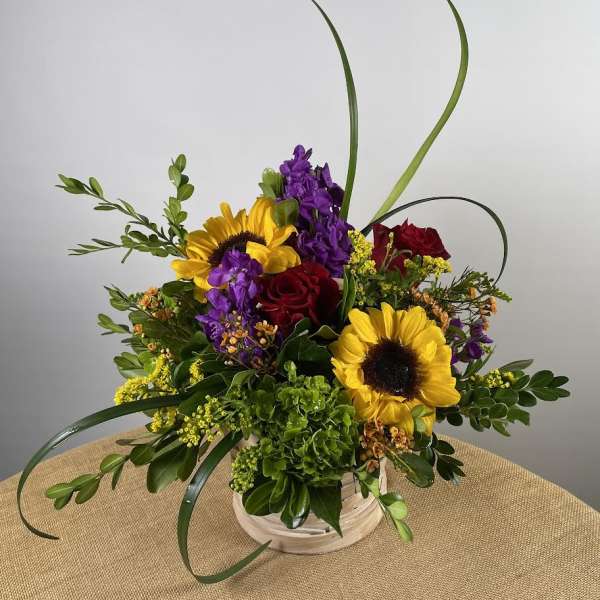Bouquet of sunflowers, red roses, and purple flowers in a white basket