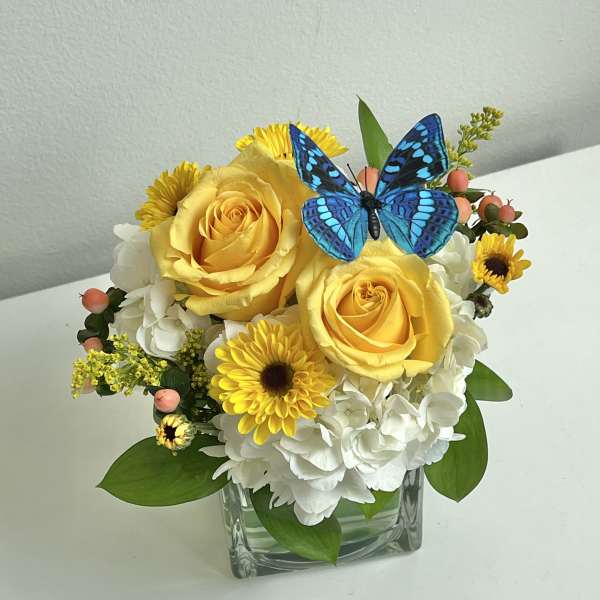 Yellow roses and white hydrangeas in a glass vase with a blue butterfly accent