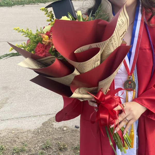 Graduate holding a wrapped bouquet of mixed flowers with a red ribbon
