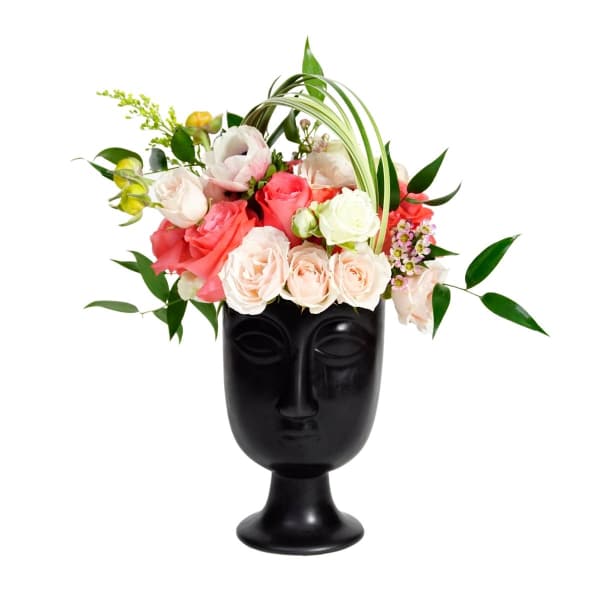 Pink and white roses arranged in a black face-shaped vase