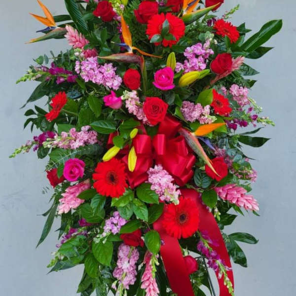 Tall standing floral spray with red roses, gerberas, and tropical blooms