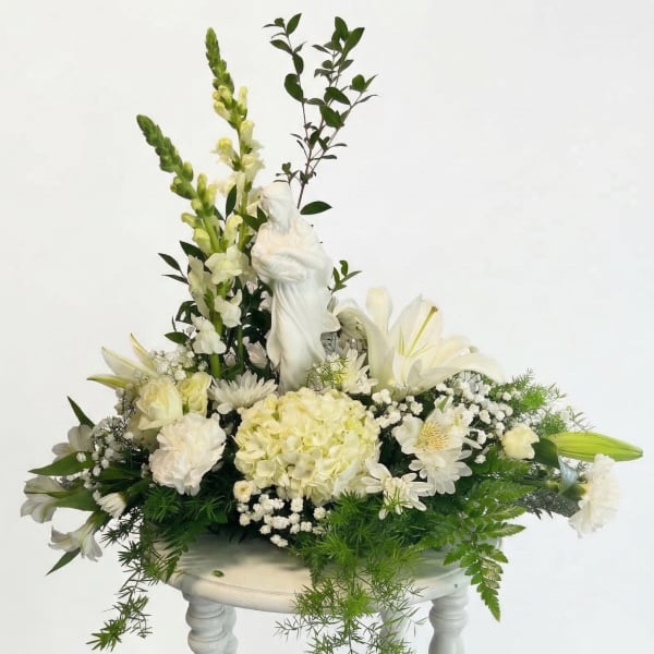 White floral arrangement with a religious statue in the center
