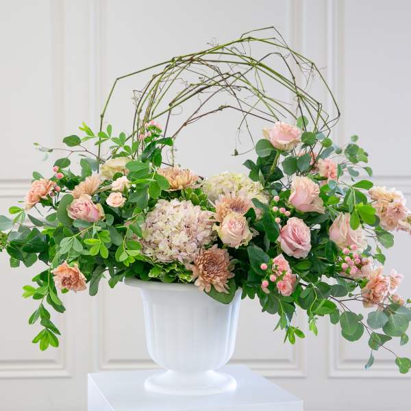 Large blush and peach flower arrangement in a white urn with arching branches