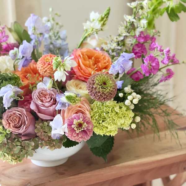 Mixed bouquet of roses, zinnias, hydrangea, and lavender flowers in a white bowl vase