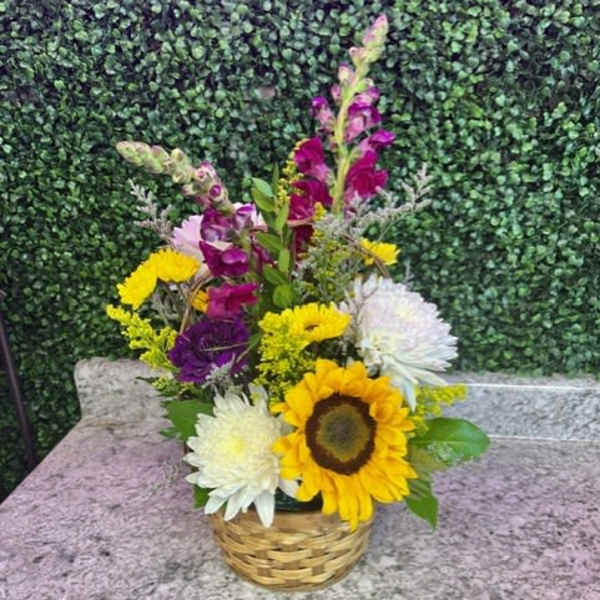 Mixed bouquet in a woven basket with sunflowers and white and purple blooms